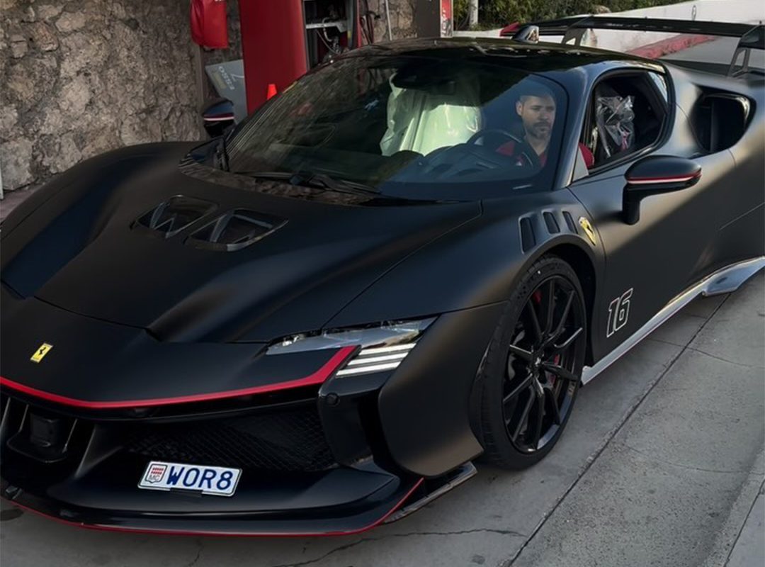 A man sits in a parked, black sports car with red accents, mirroring the sleek design of a Ferrari SF90 XX. The Monaco air complements his customized license plate, exuding an aura reminiscent of Charles Leclerc's racing finesse.