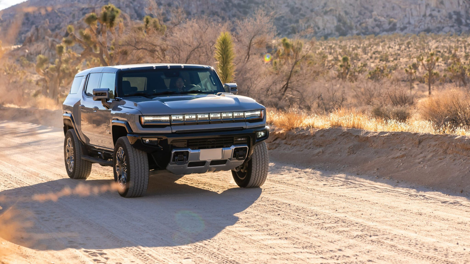 A Hummer EV SUV navigates a dusty desert road, searching for solace amidst the breathtaking mountainous landscape.