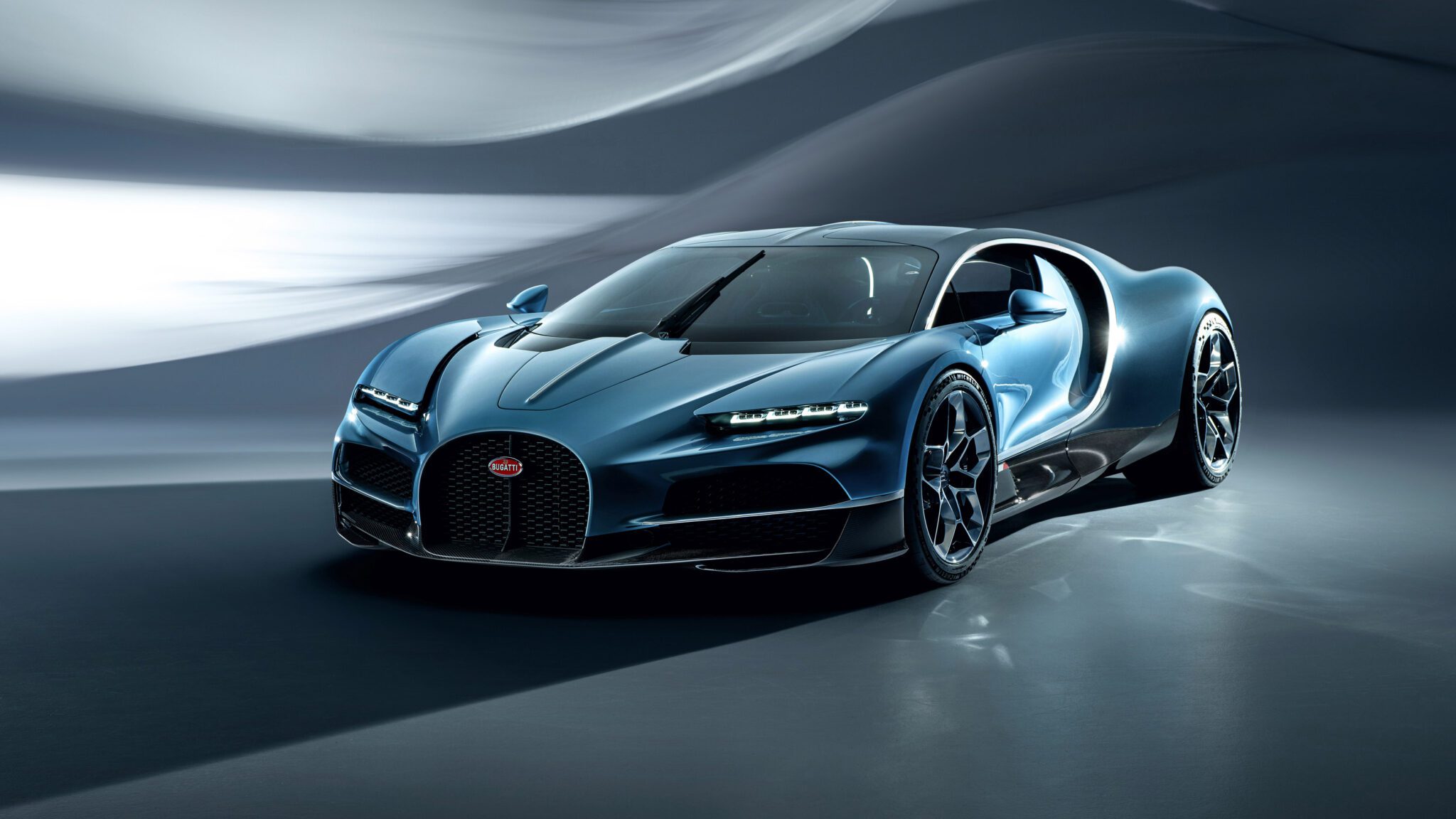 A sleek blue Bugatti sports car with a modern design is parked indoors, featuring next-century aerodynamic curves and black alloy wheels.