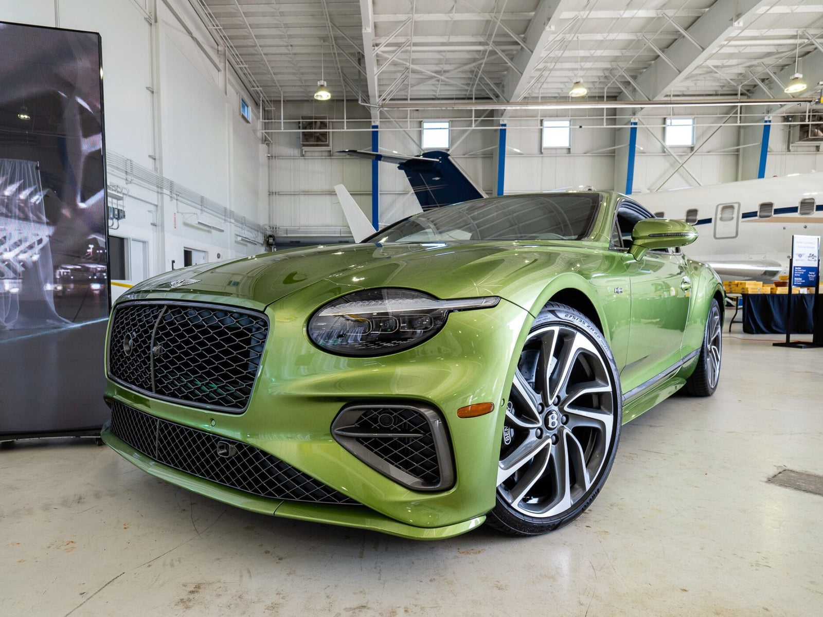 A green luxury Bentley Denver is parked indoors near a jet, showcased with sleek, modern styling and large alloy wheels, embodying the sophistication found in the duPont REGISTRY.