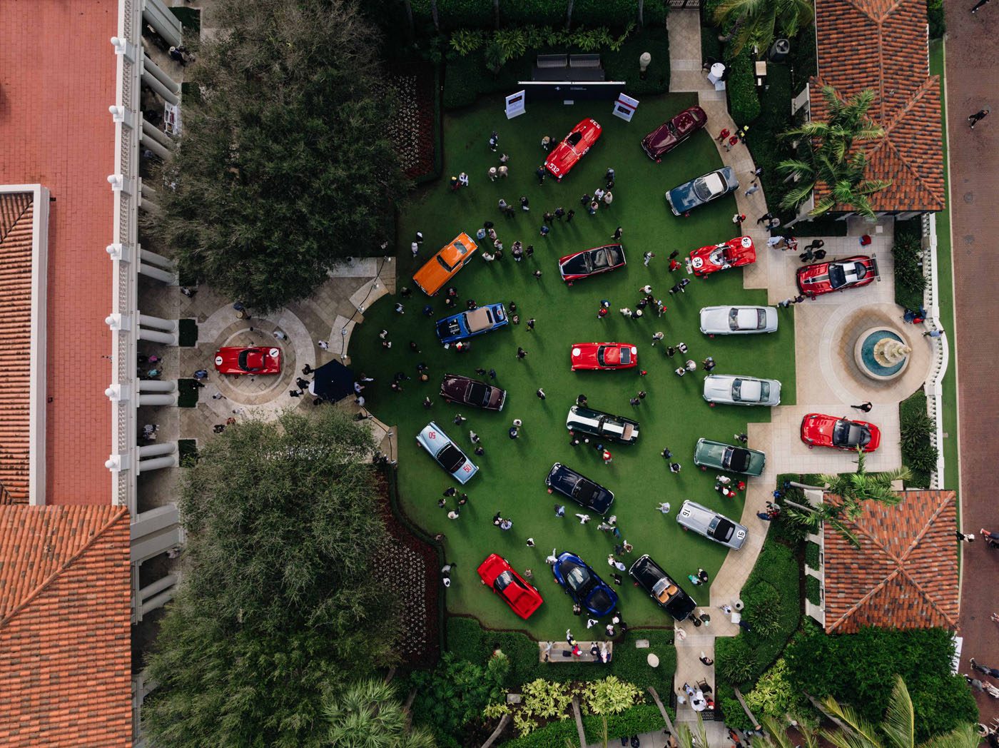 Aerial view of the Cavallino Classic car show in Palm Beach, featuring colorful cars on a green lawn surrounded by buildings and trees, with people walking and gathering—get ready for 2026 tickets.