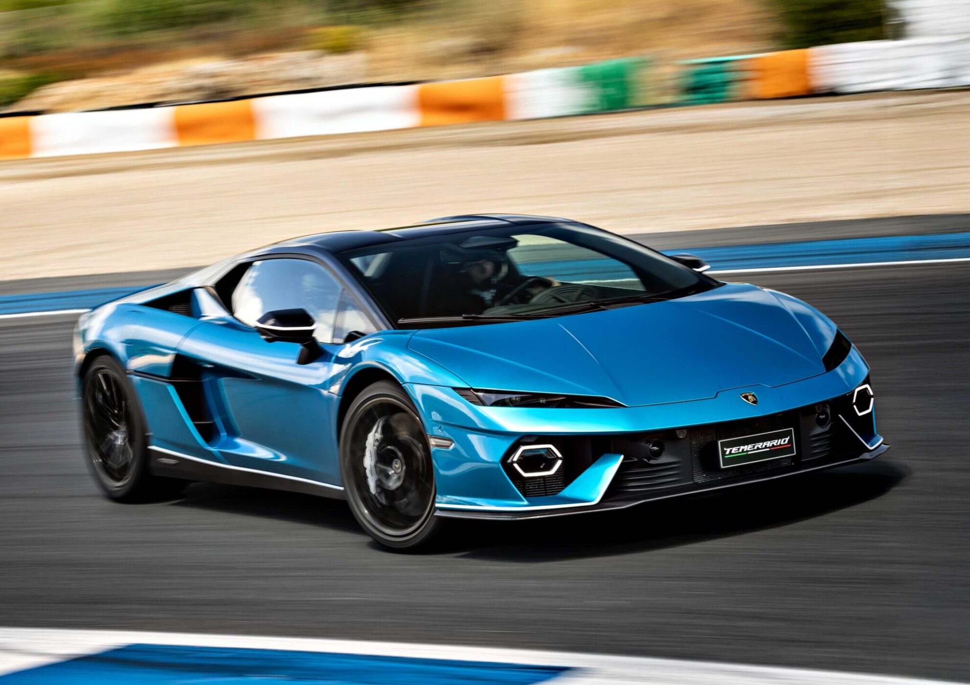 A blue V12 Revuelto Lamborghini is driving on a racetrack with a blurred background, indicating motion.