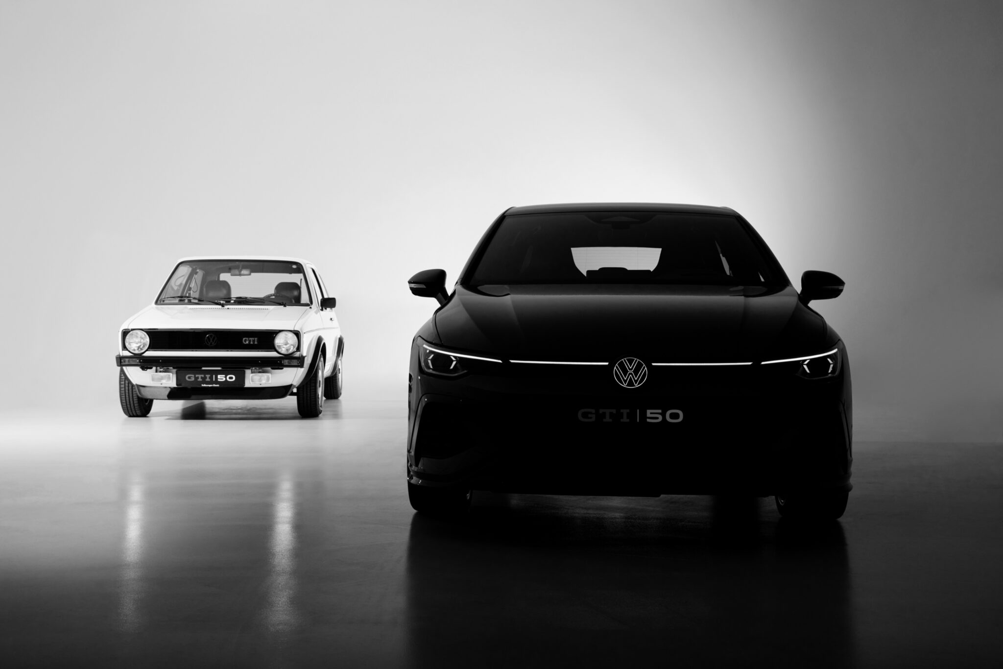 A black and white photo shows the original hot hatch, a classic Volkswagen Golf GTI, on the left and a modern Volkswagen GTI on the right, both facing forward in a studio setting.