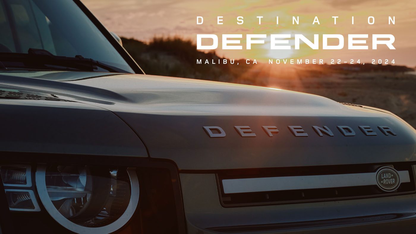Close-up of a Land Rover Defender with "Destination Defender, Malibu, CA, November 22-24, 2024" text overlay against a stunning Malibu sunset backdrop.