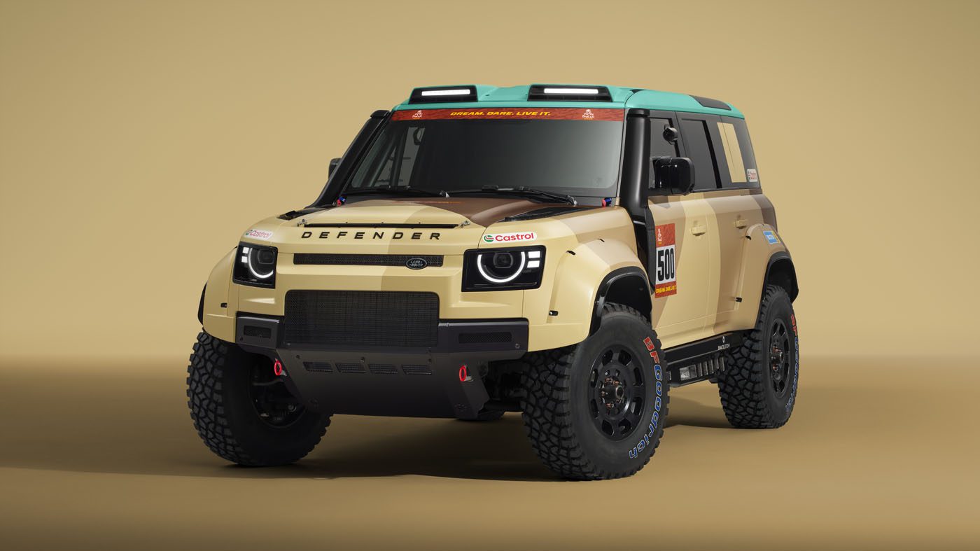 Beige and brown off-road Defender D7X-R with racing livery, rally decals, roof lights, and rugged tires, displayed in a studio setting with a plain beige background.