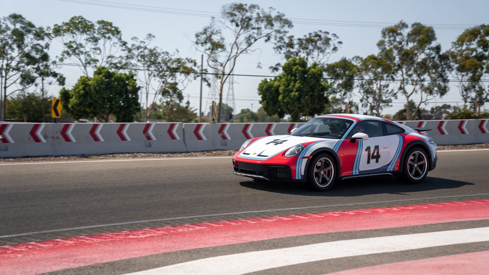 A sports car with the number 14 is racing on a track with trees and barriers in the background.