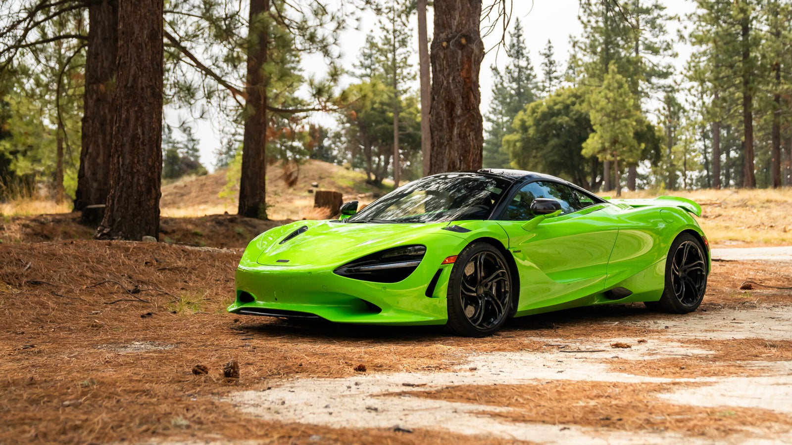 A bright green sports car is parked on a dirt path surrounded by tall pine trees in a forested area.