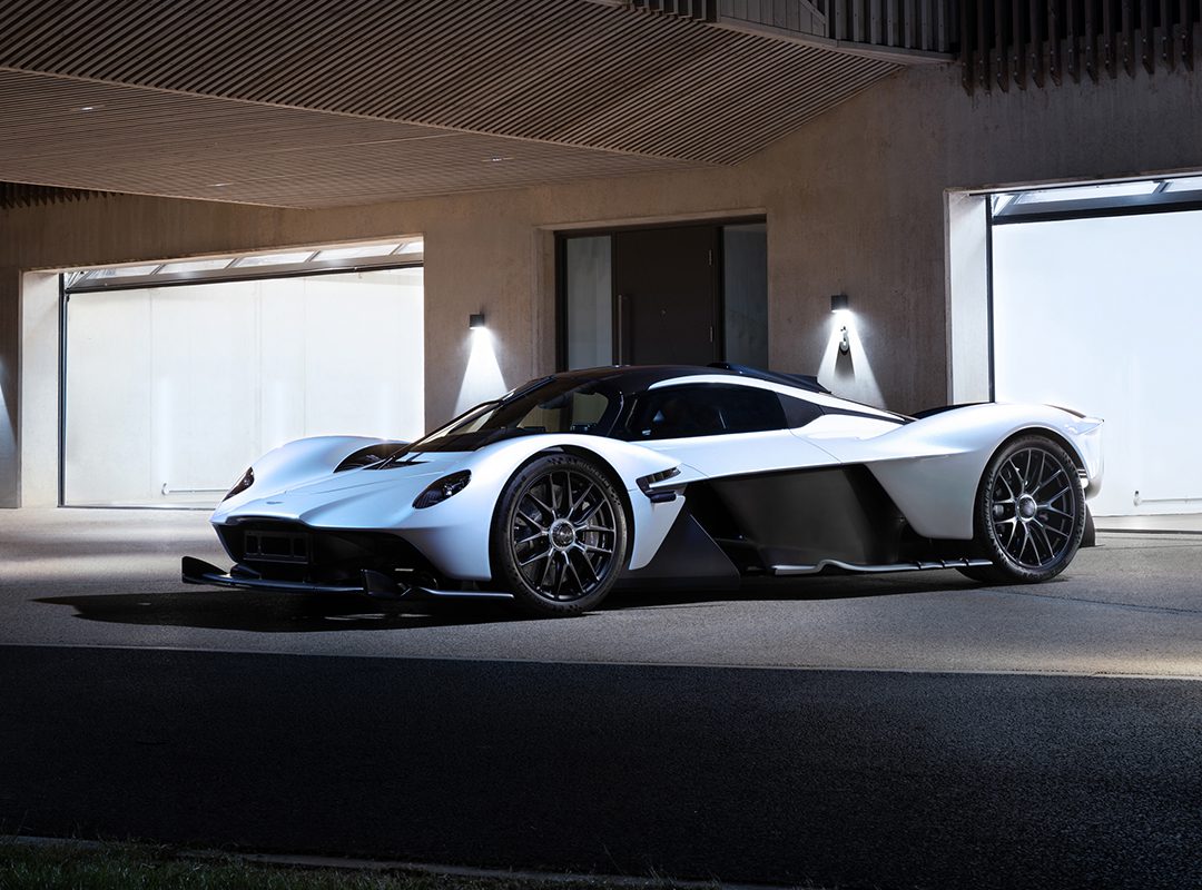 A sleek white and black Aston Martin Valkyrie with aerodynamic features is parked in front of a modern building at night, reminiscent of something Daniel Ricciardo might drive to an exclusive auction.