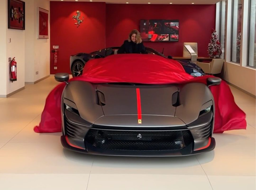 A person unveils a sleek, black sports car with red accents in a showroom.