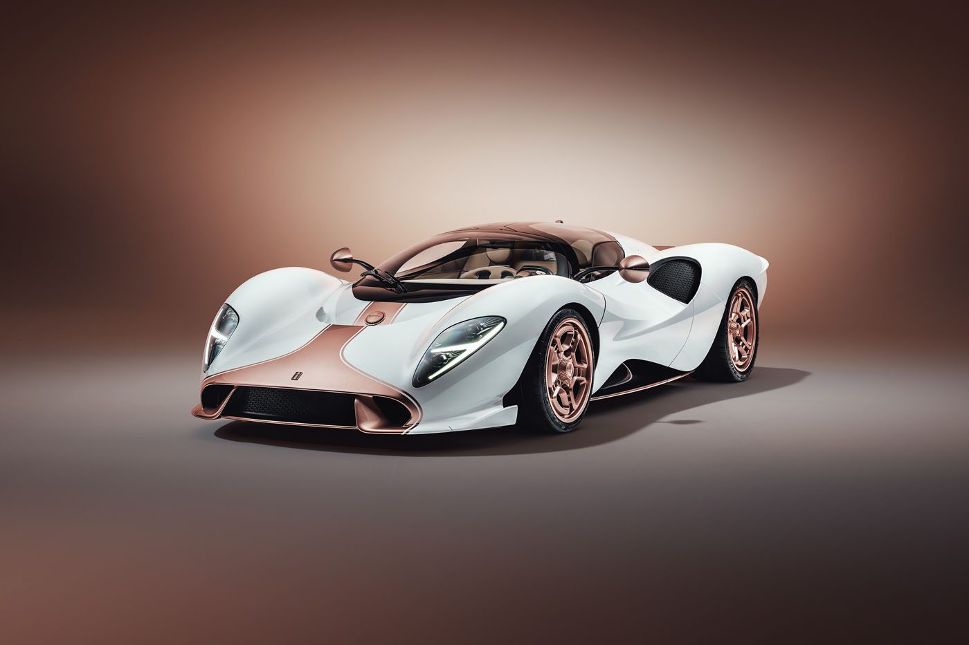 A white and rose gold De Tomaso P72 luxury sports car with a sleek, aerodynamic design is displayed in a studio setting with a neutral background, showcasing its production-spec elegance.