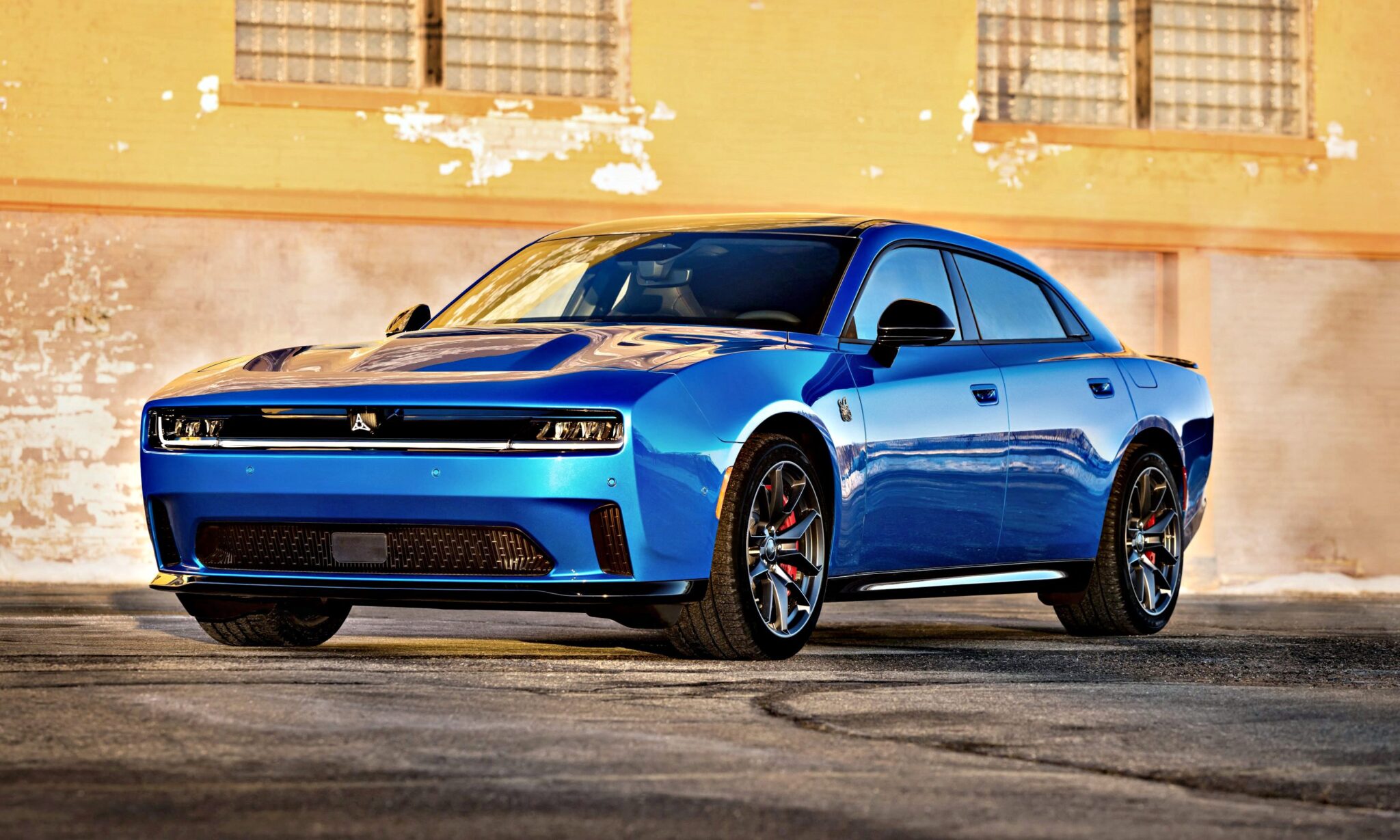A blue modern sports sedan, inspired by the Four-Door Dodge Charger Daytona, with a sleek design is parked in front of a textured, yellow-painted brick wall—there's more to this muscle car sedan than meets the eye.
