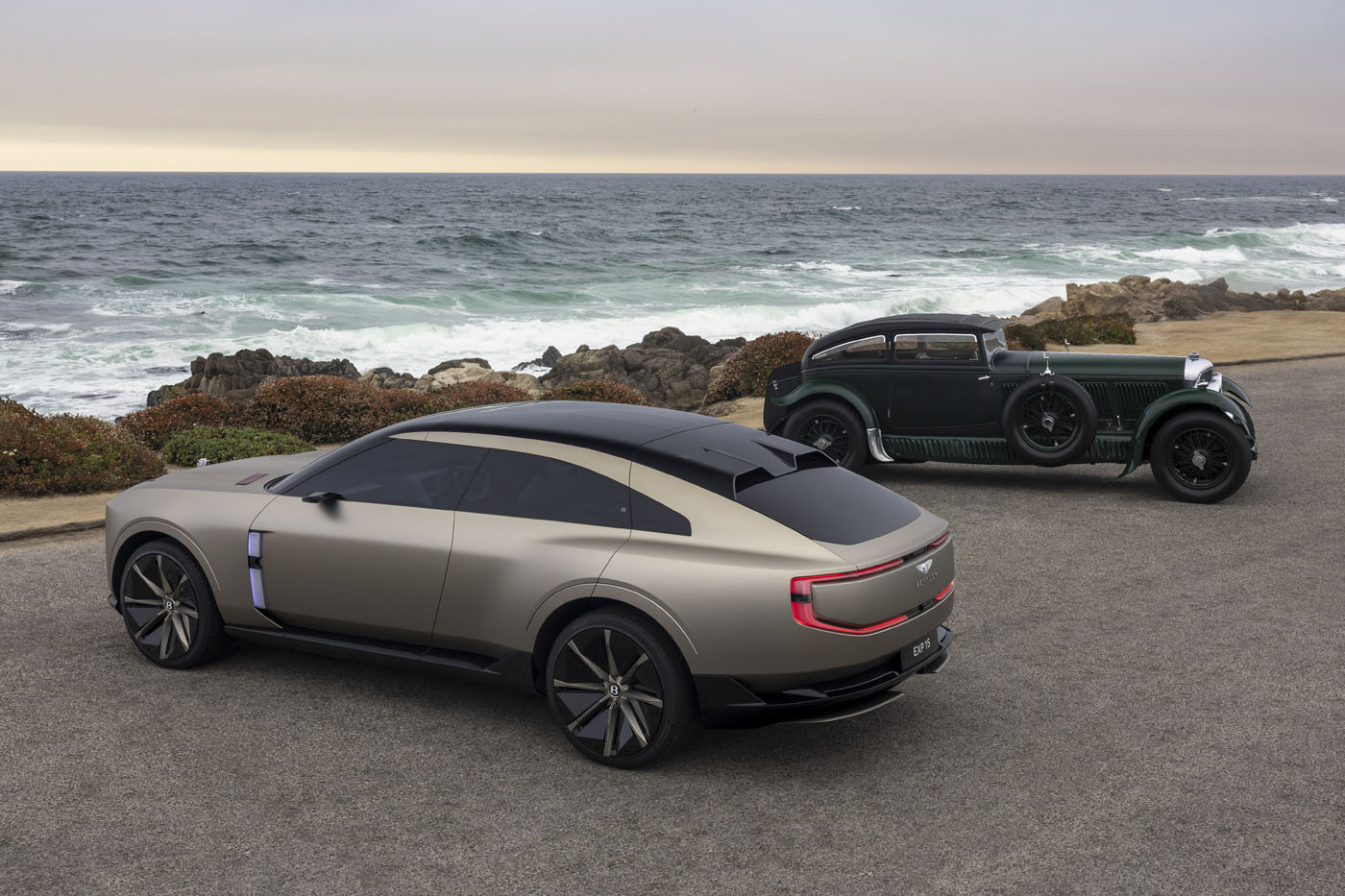 A Bentley EXP 15 Concept and a vintage car are parked on a coastal road near Pebble Beach, with the ocean and rocky shoreline providing a stunning backdrop.