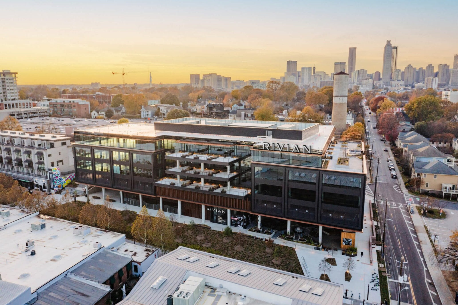 Aerial view of Rivian’s modern, multi-story Atlanta Headquarters with large windows and rooftop terraces, set in an urban neighborhood at sunrise with the city skyline in the background.