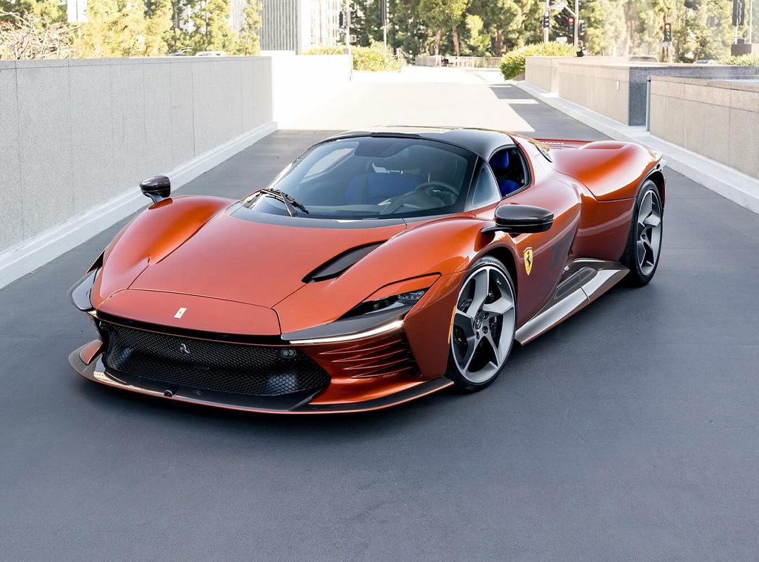 A sleek, orange Ferrari sports car with a modern design is parked on a paved surface, surrounded by the luxury of Beverly Hills' urban architecture and greenery.