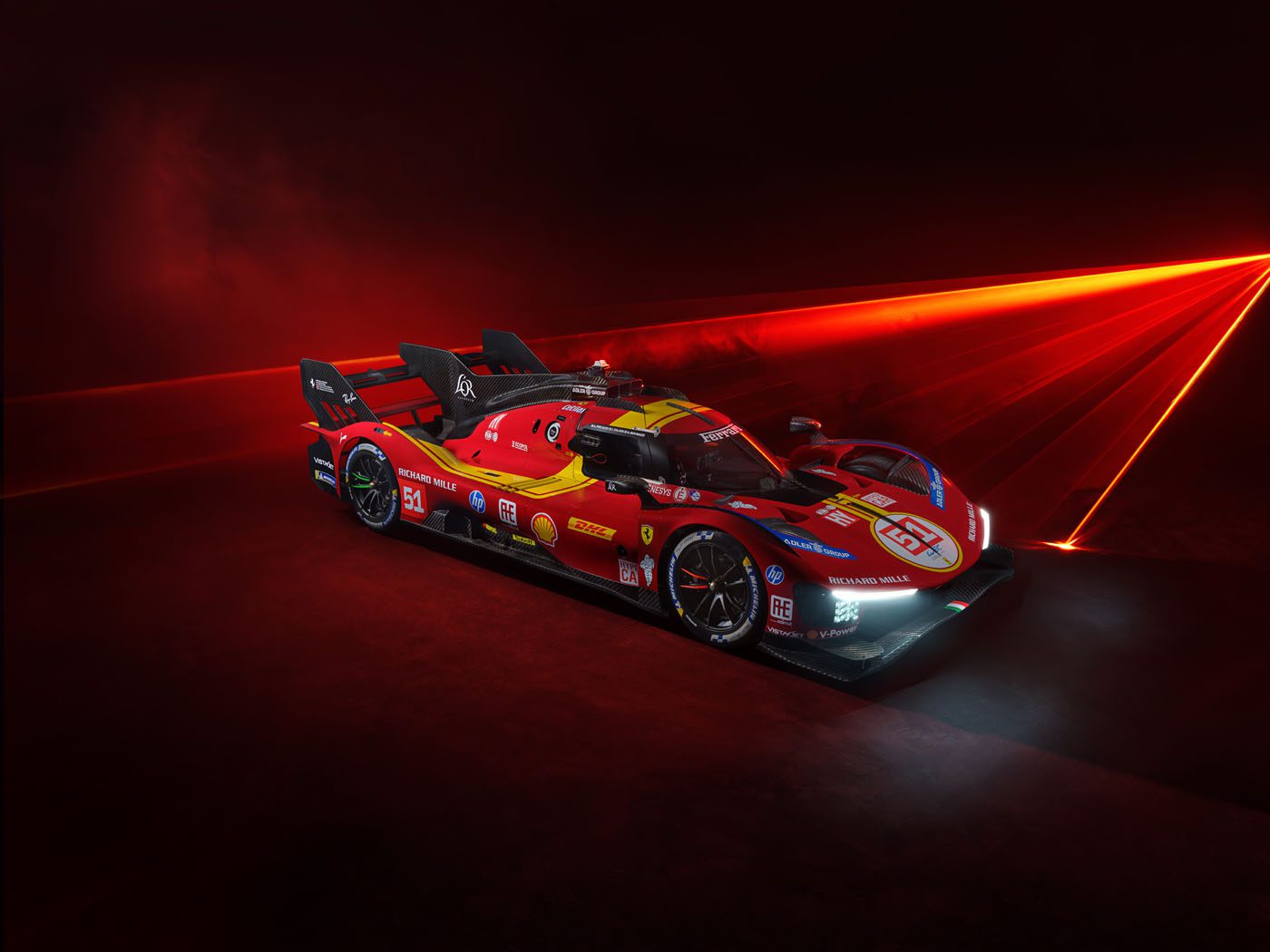Beneath the intense red lighting, a striking red and yellow Ferrari 499P Hypercar proudly displays its sponsor logos, showcasing its sleek design.
