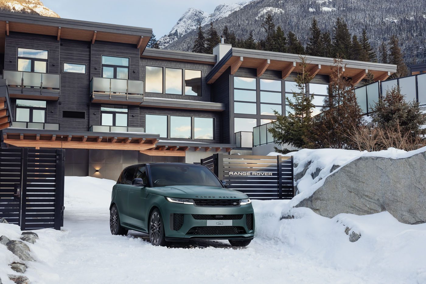 A green Range Rover Sport SV from the London Collection sits elegantly on a snowy driveway in front of a modern house, framed by majestic snowy mountains and towering trees.