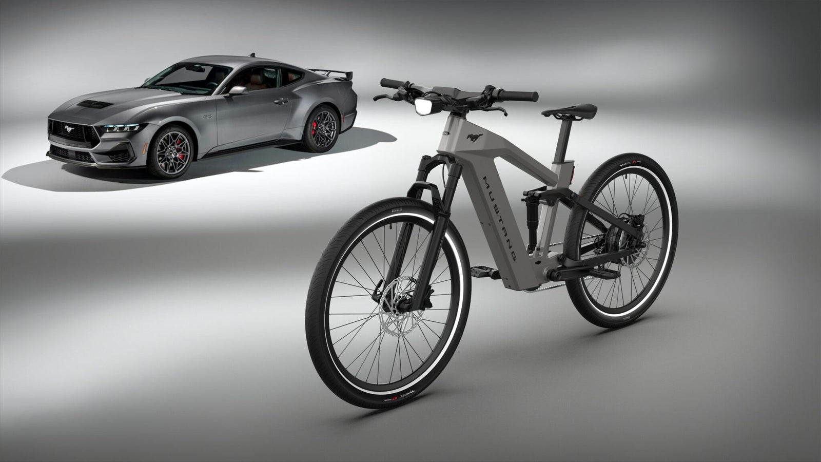 A sleek gray electric bike from the Ford eBikes collection stands in the foreground, while a gray sports car reminiscent of a Mustang looms in the background against a minimalist studio backdrop.