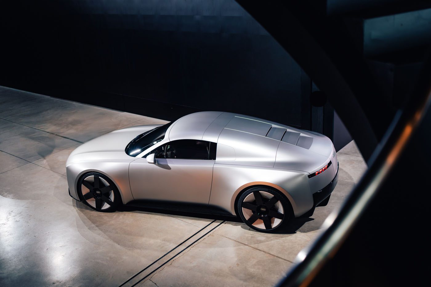 A sleek silver Audi Concept C with a futuristic design is parked indoors on a concrete floor in London, viewed from an elevated angle.