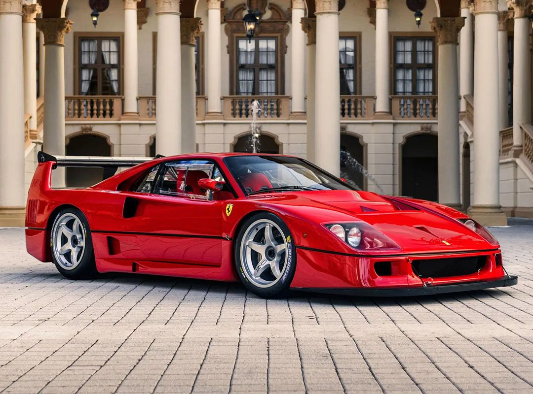 A red Ferrari F40 LM is parked on a cobblestone driveway in front of an ornate building with columns and arches, reminiscent of the elegance seen at RM Sotheby's Monterey Auction.