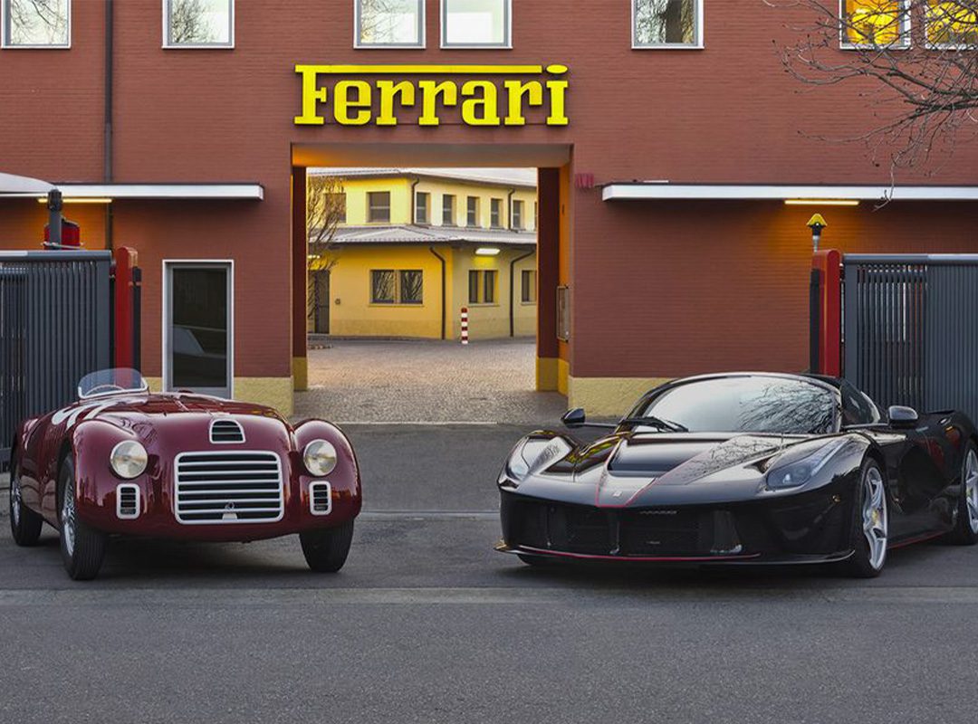 Two Ferrari cars, one vintage and one modern, are parked outside a red Ferrari building with a yellow sign, showcasing the brand's legacy of product innovation.