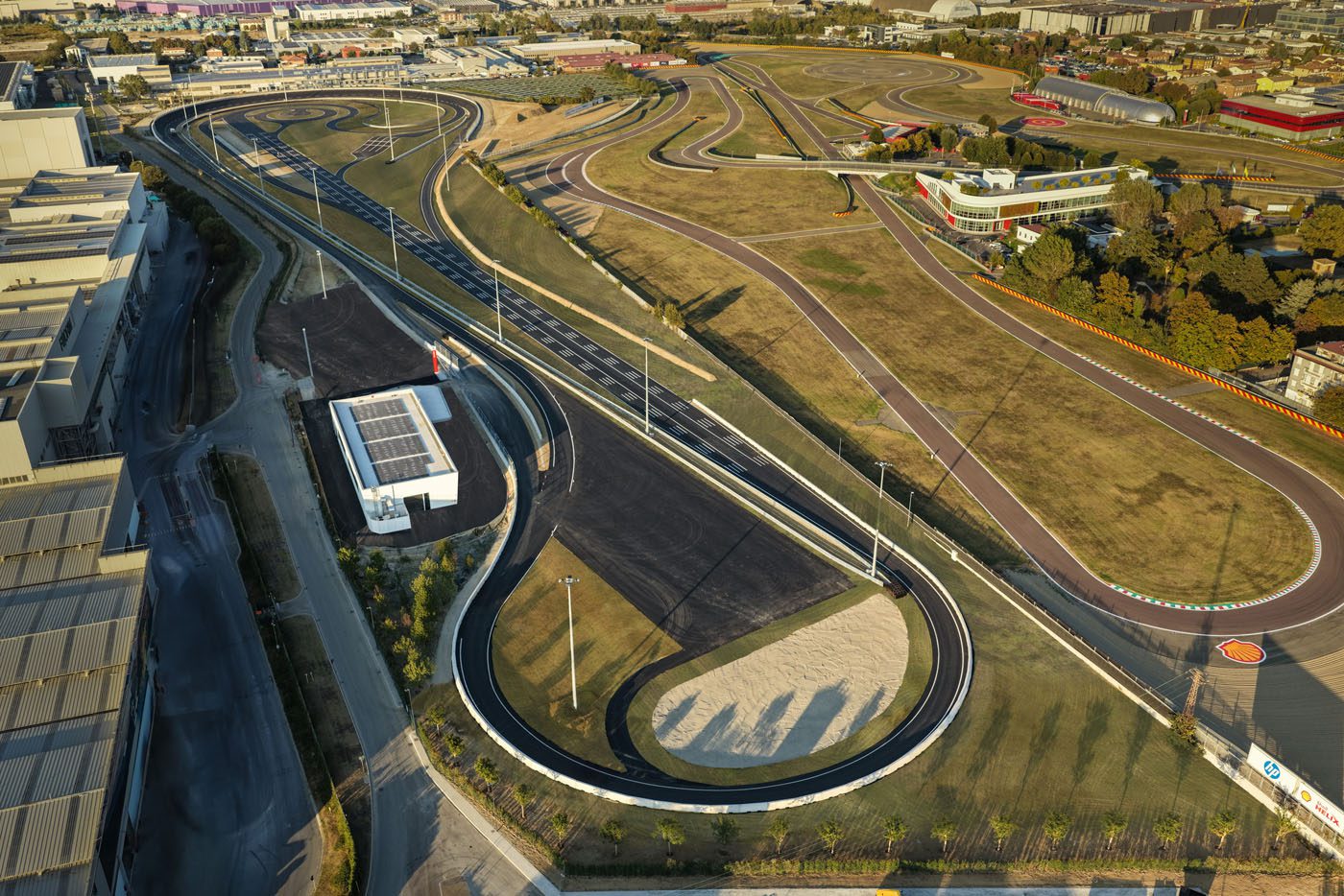 Aerial view of the Ferrari e-Vortex Test Track, a large, winding test track with multiple curves and paved roads, surrounded by grassy areas and nearby buildings.