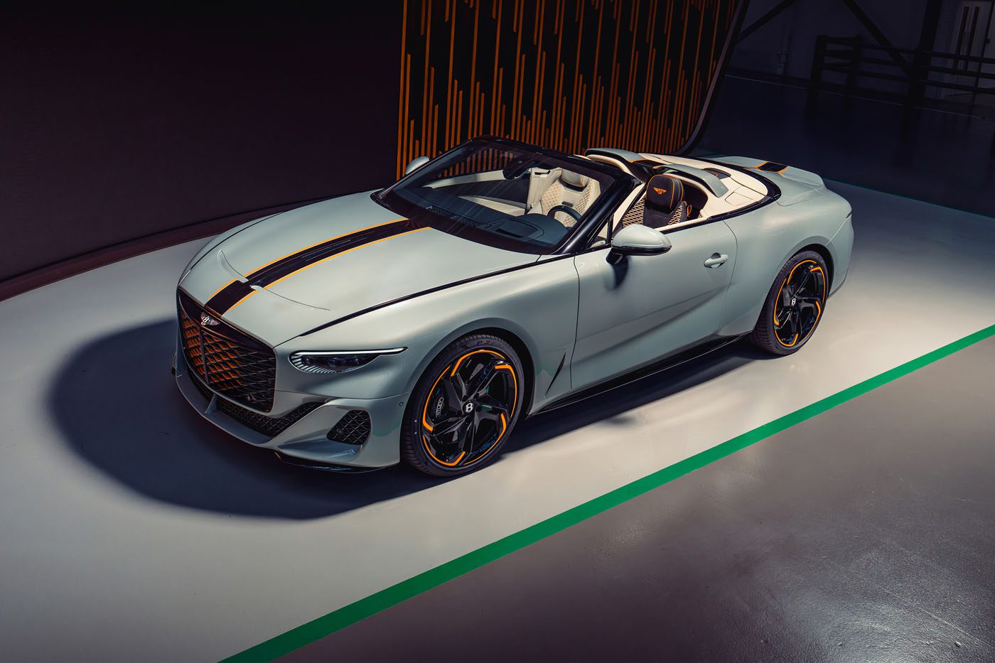 A silver convertible sports car with orange and black accents is parked indoors on a gray floor with a green line.