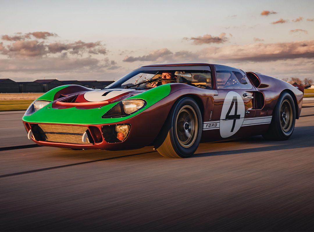 A vintage Ford GT40, boasting the number 4 and painted in vibrant shades of green, red, and brown, roars down the track beneath a cloudy sky. This iconic gem is set to turn heads at RM Sotheby's Miami Auction.