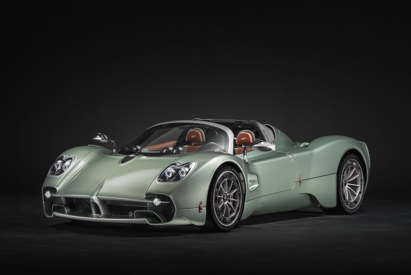 A matte sage green Pagani sports car with a convertible roof, silver wheels, distinctive headlights, and brown leather seats, photographed in a studio with a black background—ready for the hillclimb runs at Goodwood FoS 2025.