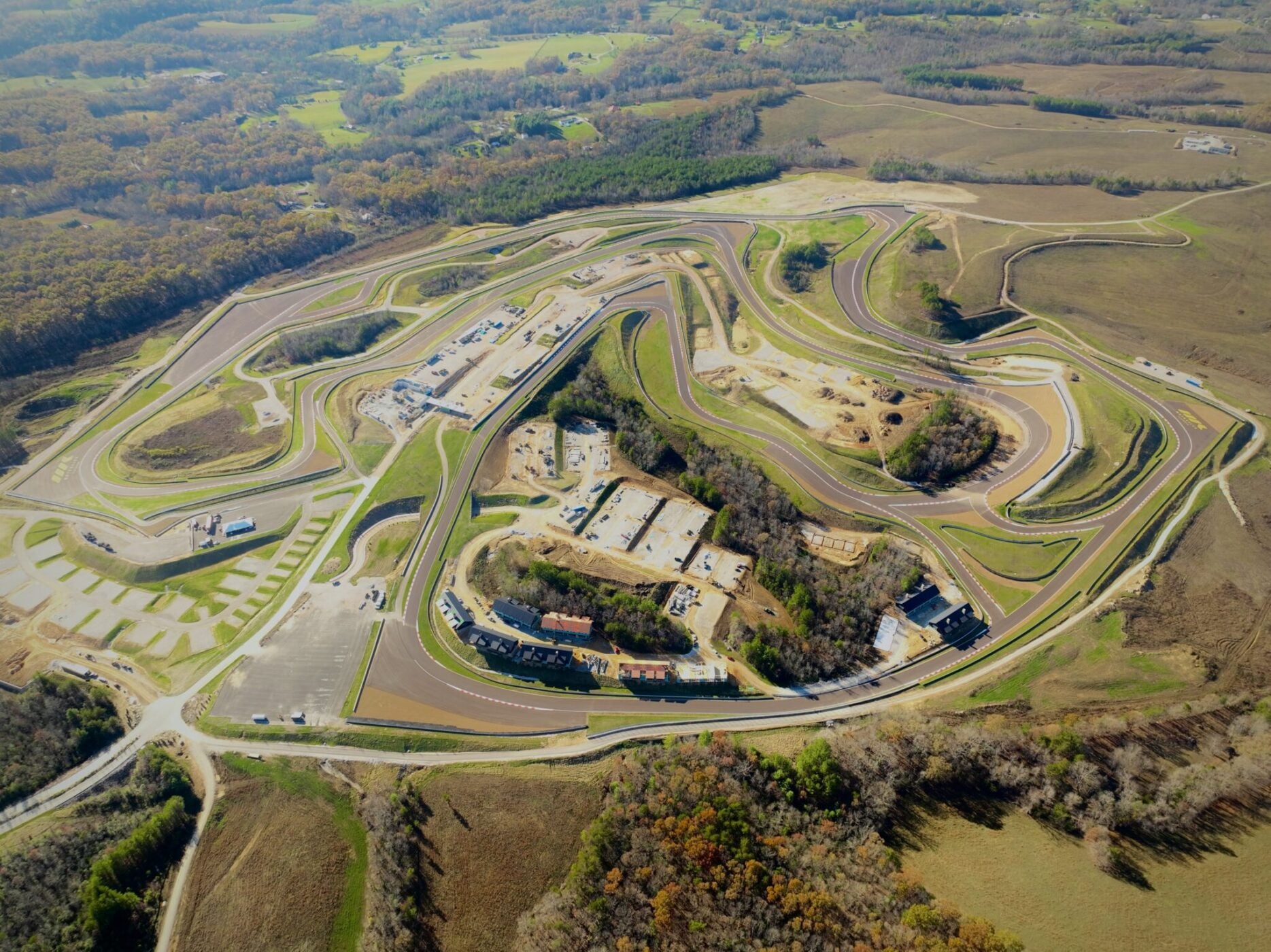 Aerial view of the Flatrock Motorclub racetrack amidst a hilly landscape, with buildings and parking areas surrounded by trees and open fields.
