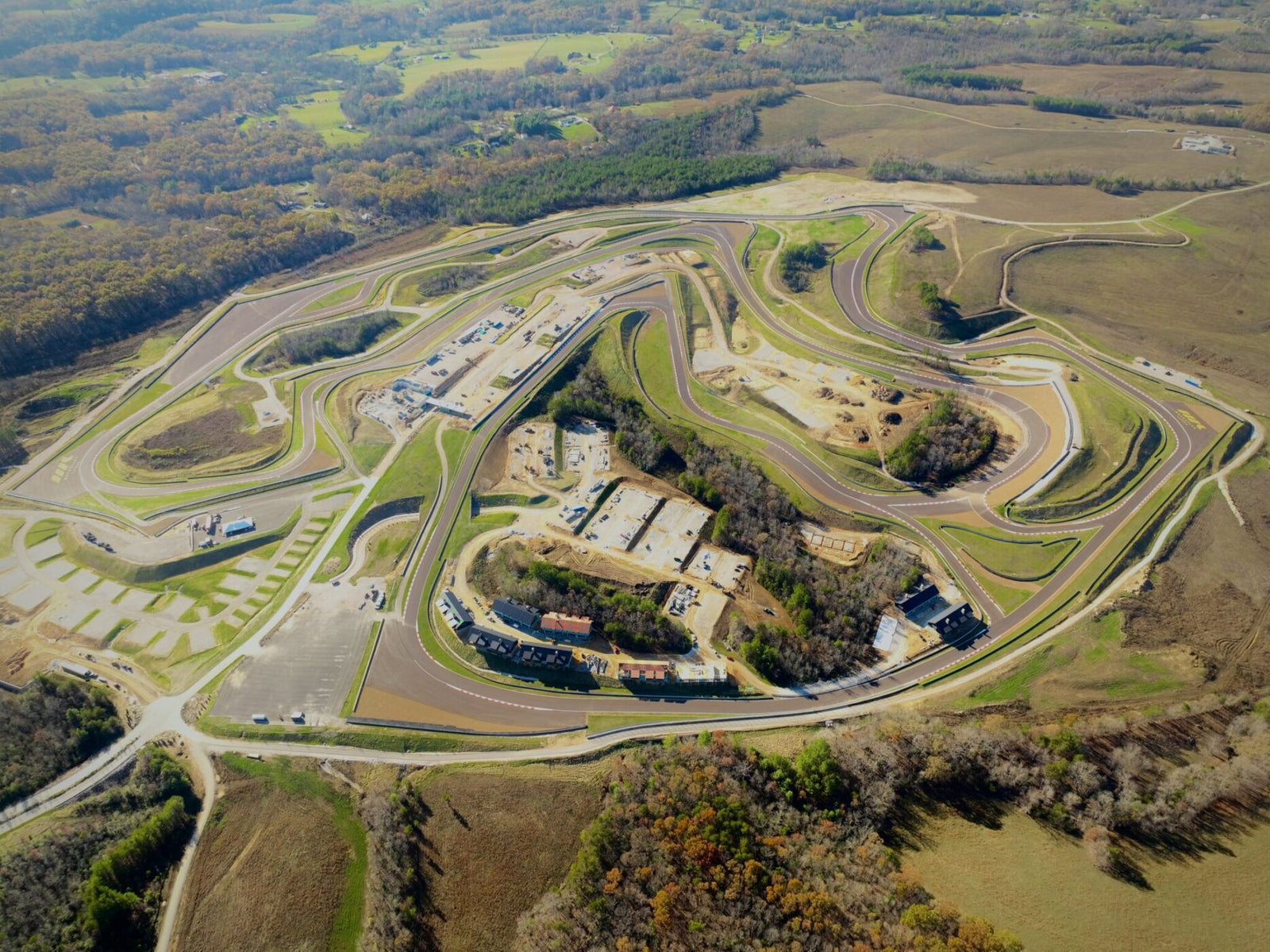 Aerial view of the Flatrock Motorclub racetrack amidst a hilly landscape, with buildings and parking areas surrounded by trees and open fields.