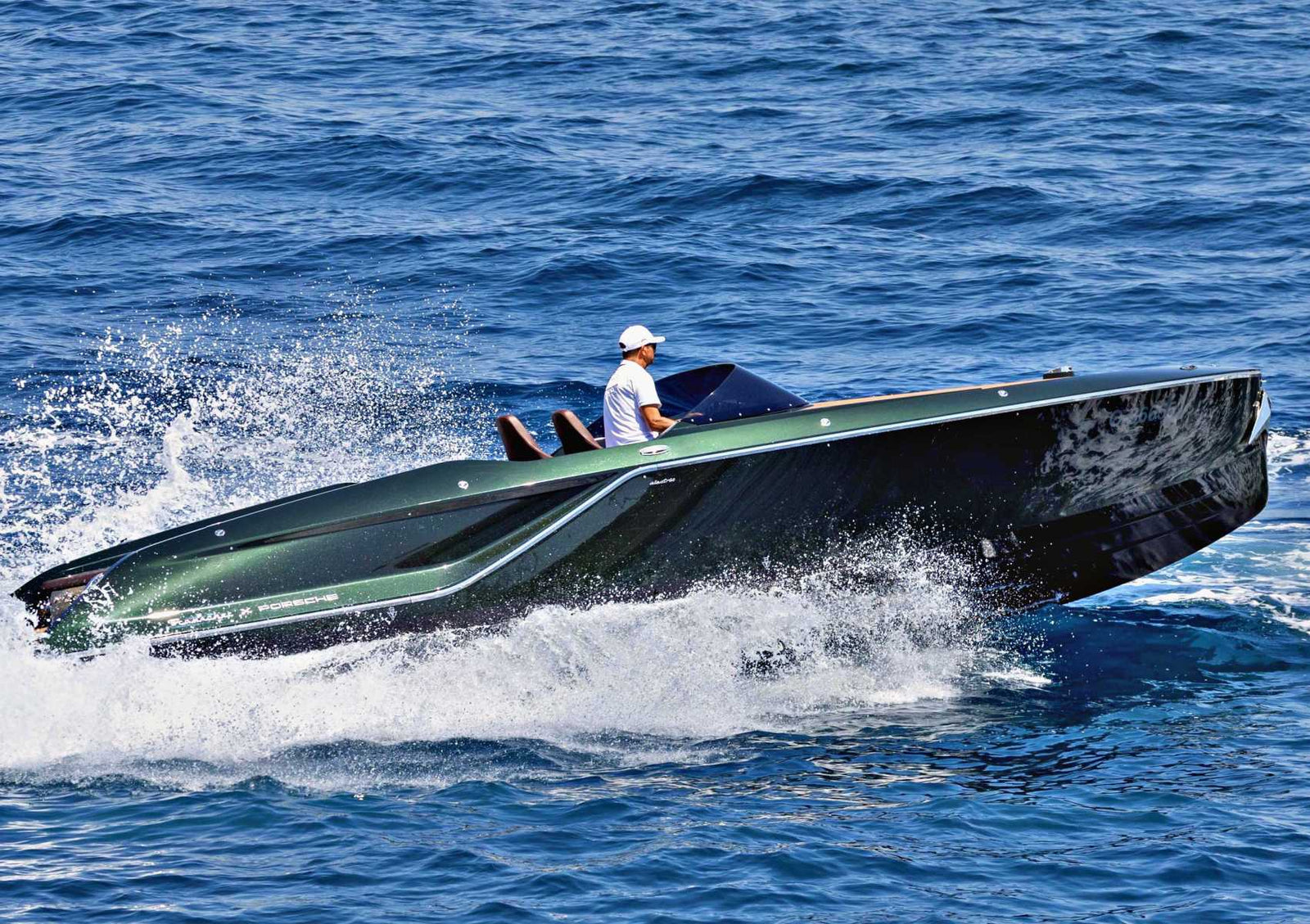 A person wearing a white cap pilots a sleek, modern Frauscher Fantom 850 speedboat at high speed across blue ocean water, creating a large spray.