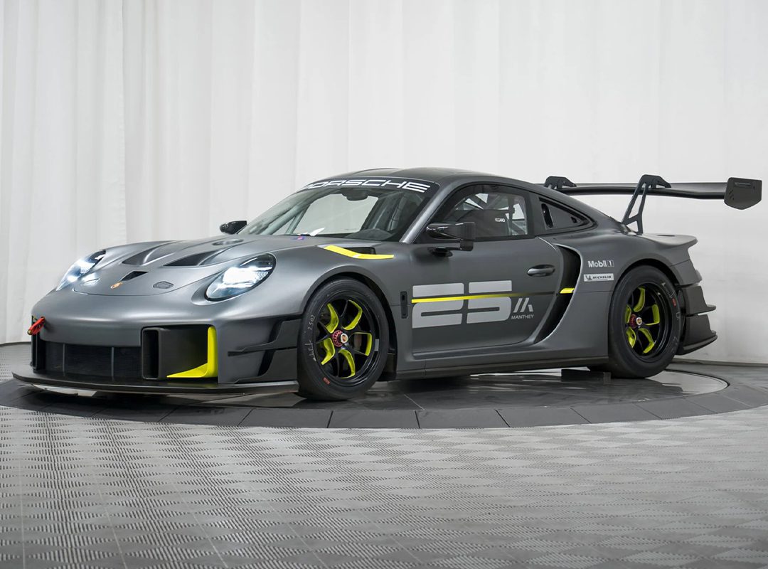 A matte gray Porsche GT2 RS Clubsport 25 race car with yellow accents, large rear wing, aerodynamic features, and the number 25 displayed on the side, is showcased in a studio setting, highlighting its race-ready design.