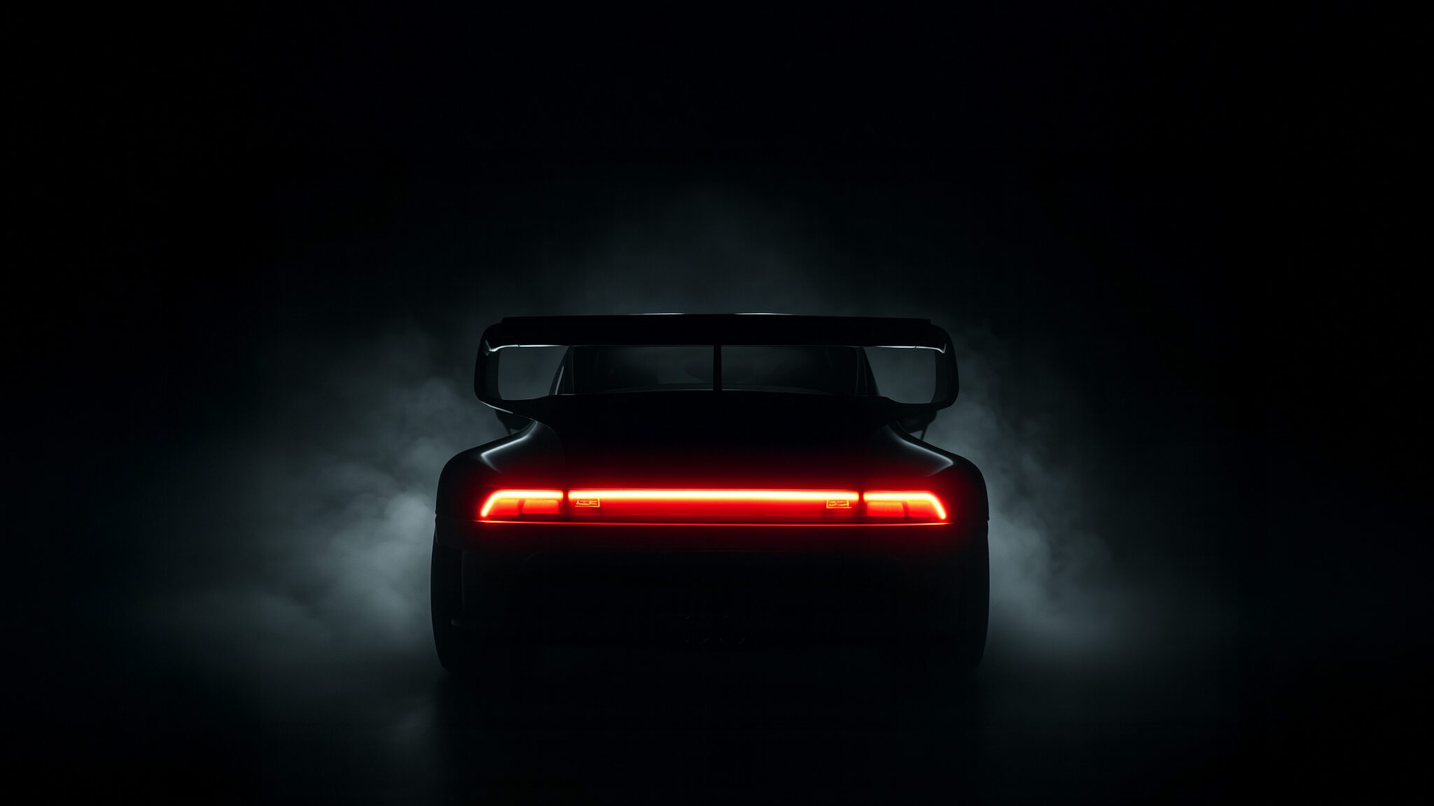 A rear view of a Slantnose-inspired sports car with a large spoiler, illuminated by its red taillight, surrounded by darkness and faint smoke—an unmistakable Gunther Werks presence at The Quail.