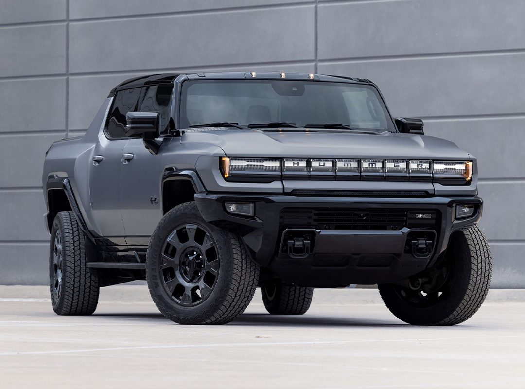 A matte black 2026 GMC HUMMER EV electric pickup truck is parked in front of a modern gray concrete wall.