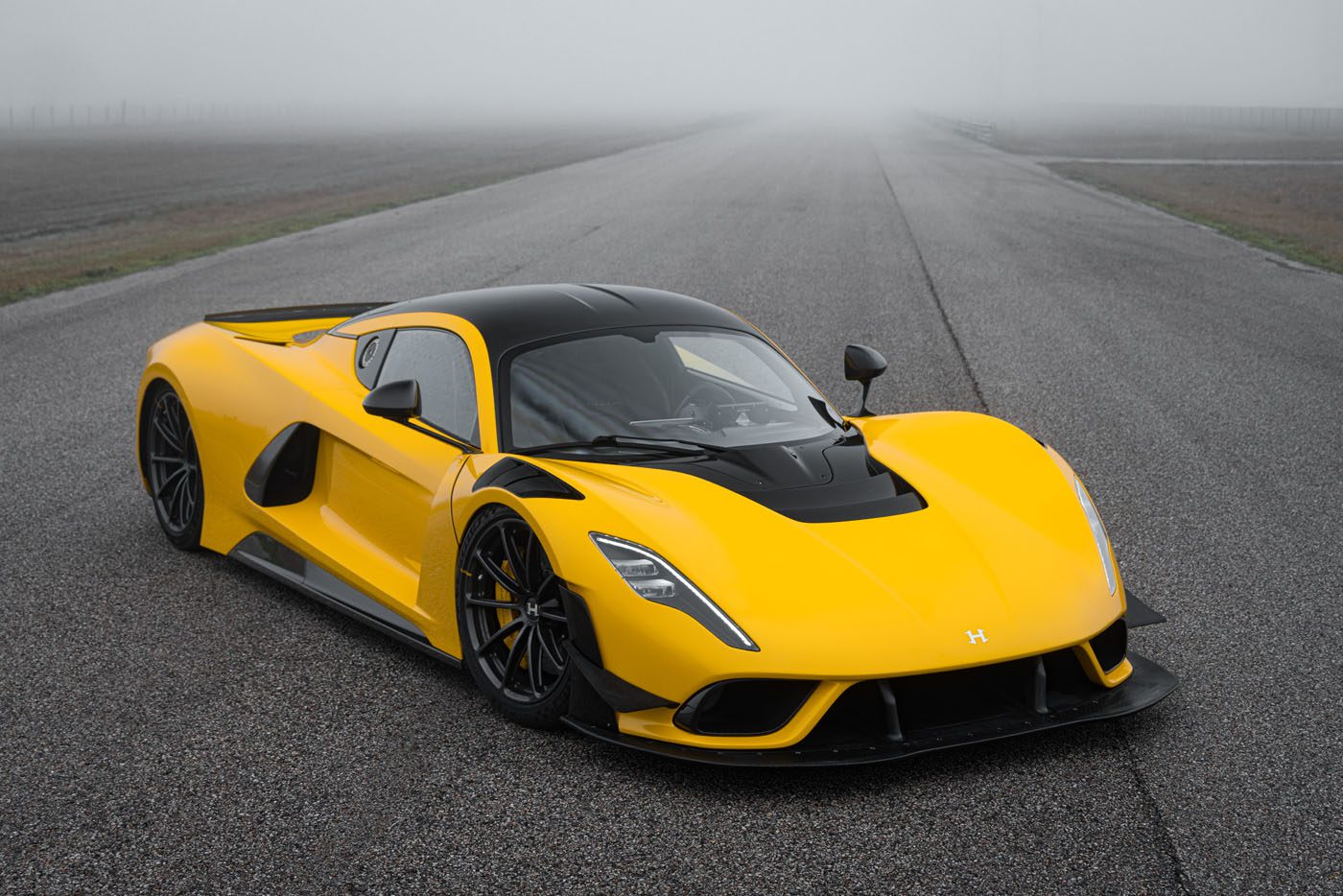 A yellow and black Hennessey Venom F5, boasting 2,031HP, is parked on an empty, foggy racetrack—an icon of speed and evolution.