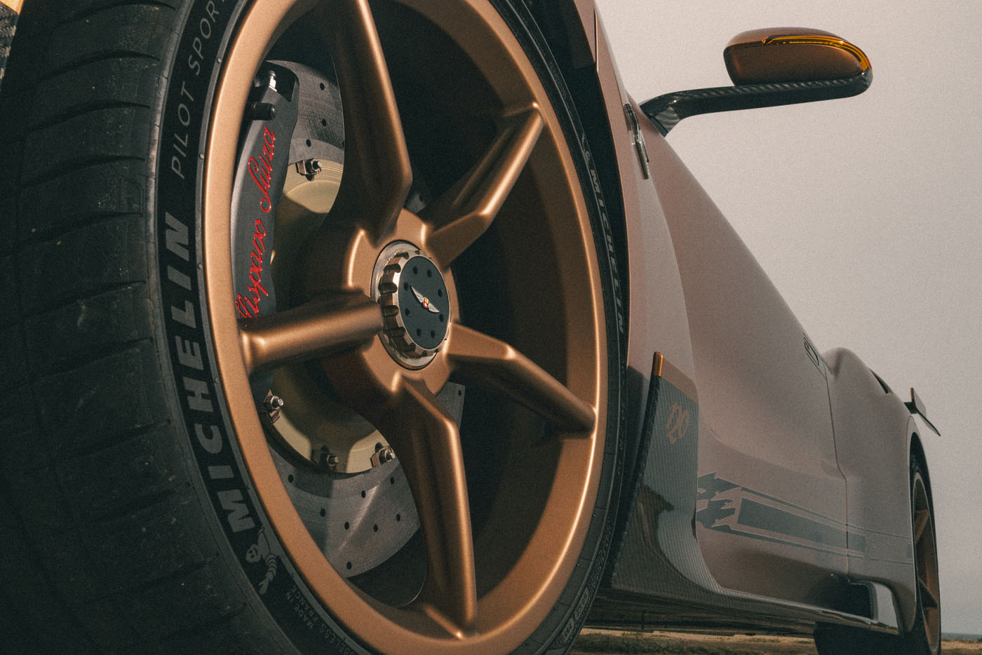 Low-angle close-up of a gold alloy wheel and tire on a Hispano Suiza sports car, highlighting brake calipers and "Michelin Pilot Sport" branding, showcasing the premium engineering of Michelin Tires.