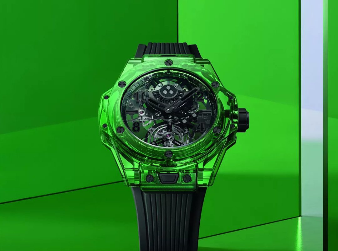 A green transparent watch from Hublot with a visible intricate mechanism and a black band, set against a bright green geometric background, epitomizes the innovation celebrated at LVMH Watch Week.