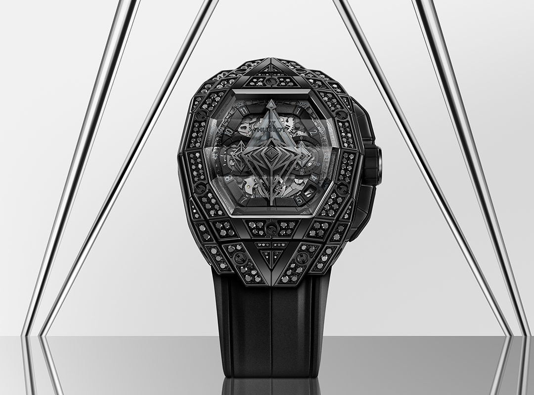 A geometric, intricately designed black watch from the Hublot Spirit of Big Bang collection features a multi-faceted bezel adorned with black diamond details, set against a modern metal triangular backdrop.