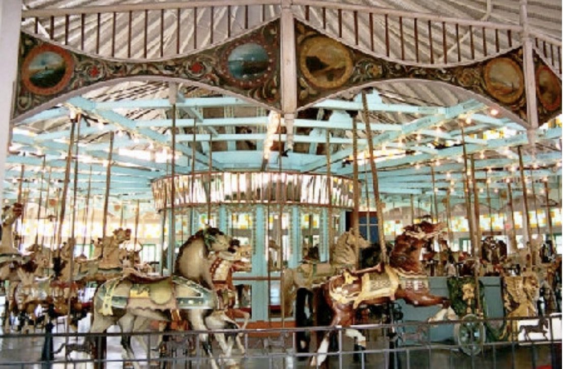 Antique carousel with elaborately painted horses and a decorative canopy under a roofed structure.