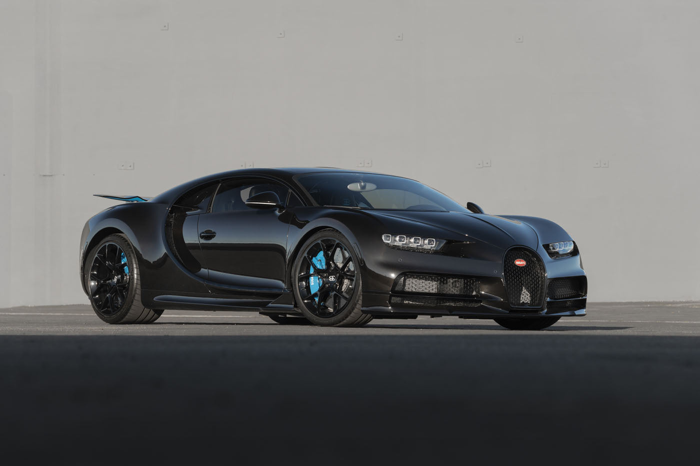 A black Bugatti Chiron sports car sits parked on a paved surface in front of a plain gray wall, soon to be showcased by Broad Arrow at the 2025 Monterey Auction.