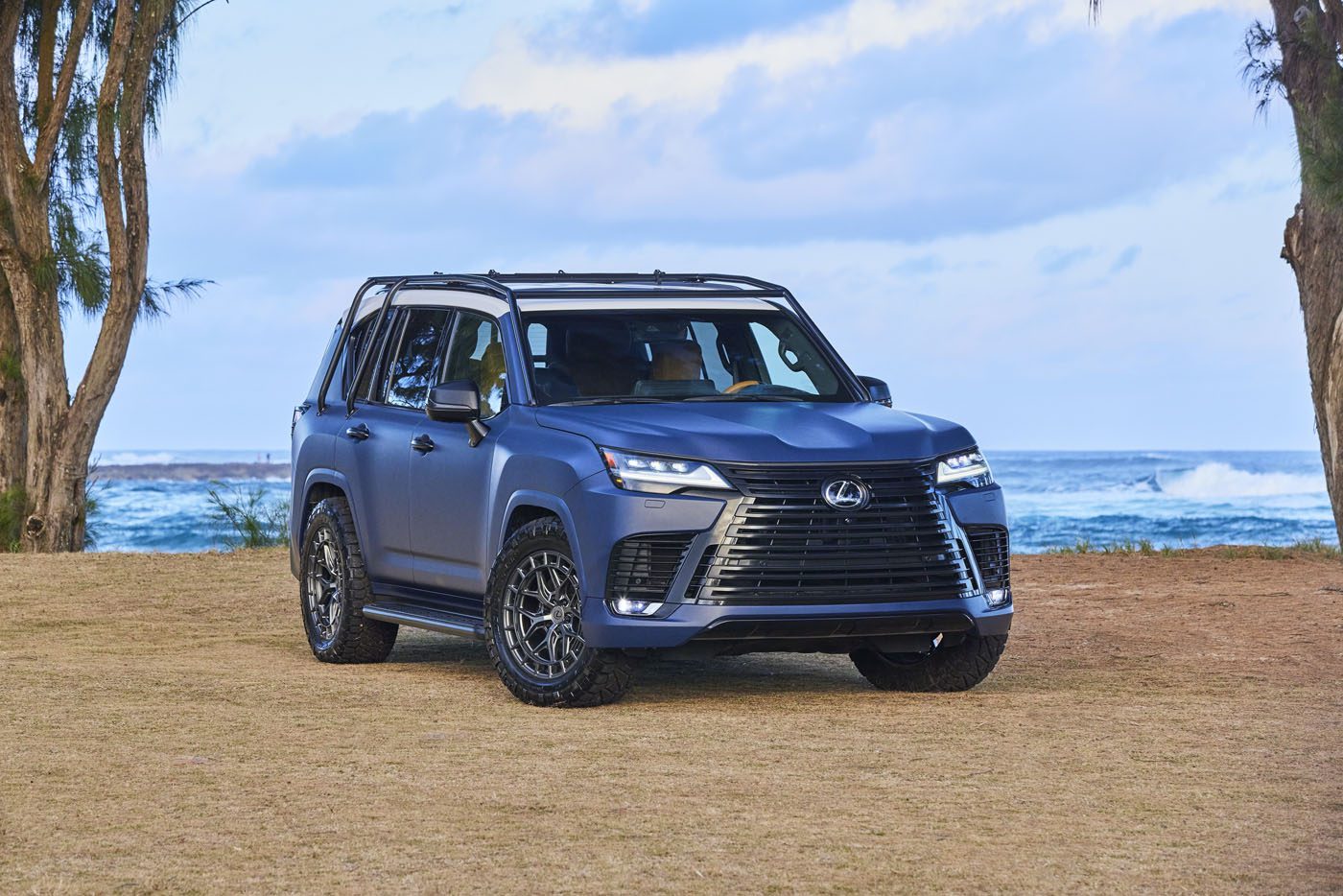 A blue Lexus SUV, the Surf LX Concept, is parked gracefully on the lush grass near the Hawaiian ocean, framed by swaying trees and crashing waves in the background.