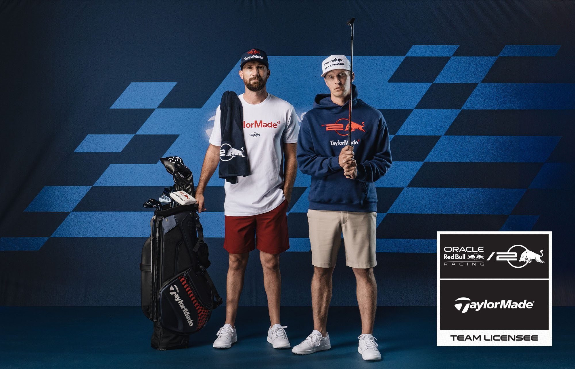 Two men in golf attire stand beside a golf bag adorned with the Pursuit Golf Collection. They wear TaylorMade branding and pose confidently in front of an Oracle Red Bull Racing backdrop, where a sign reads "Team Licensee.