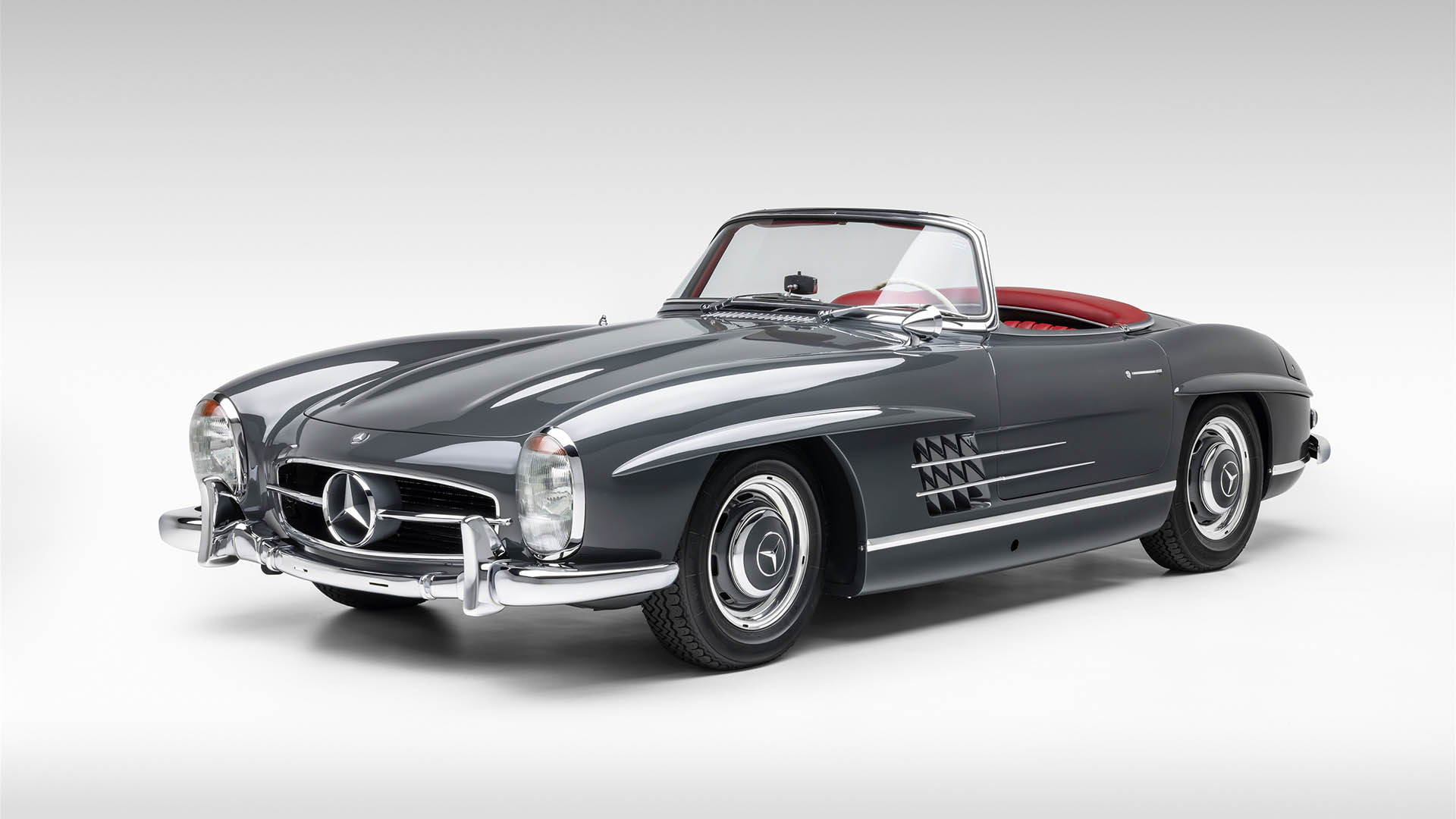 A classic grey Mercedes-Benz SLR McLaren convertible with a red interior, viewed from the front left against a plain white background—an iconic design destined for Broad Arrow’s Las Vegas 2025 event.