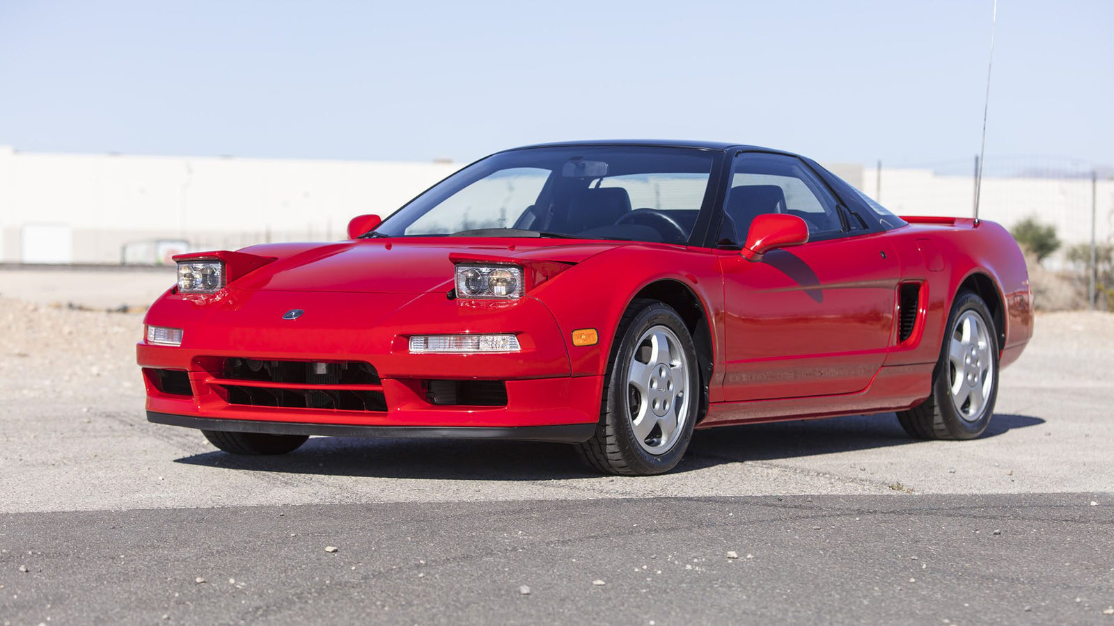 A red Ferrari SF90 Spider with pop-up headlights and silver wheels is parked on a paved surface outdoors under a clear sky, ready for Broad Arrow's Las Vegas 2025 event.