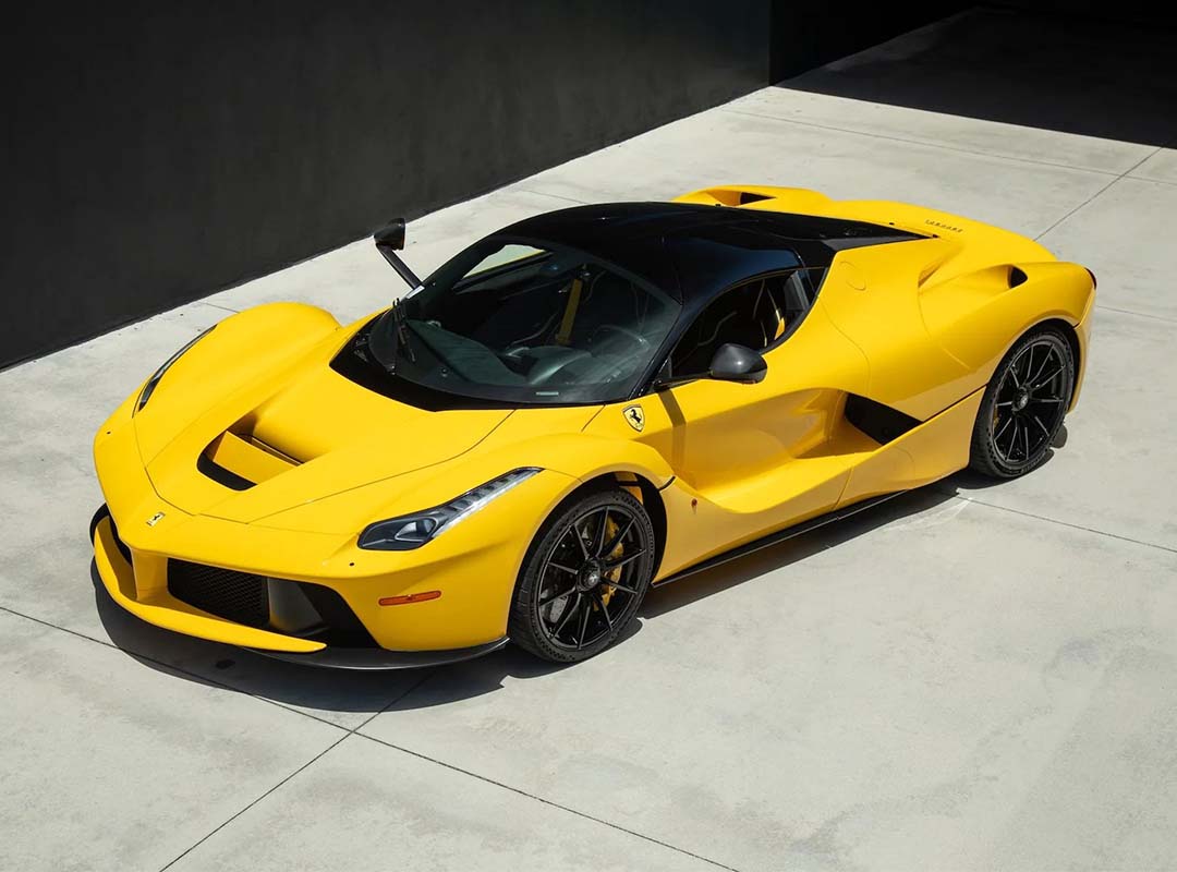 A yellow Ferrari LaFerrari hypercar is parked on a smooth, light-colored concrete surface near a dark wall.
