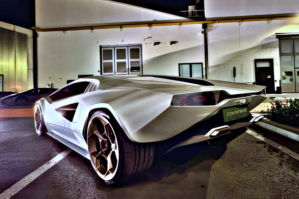 A sleek white sports car is parked at night in front of an industrial building under artificial lighting.