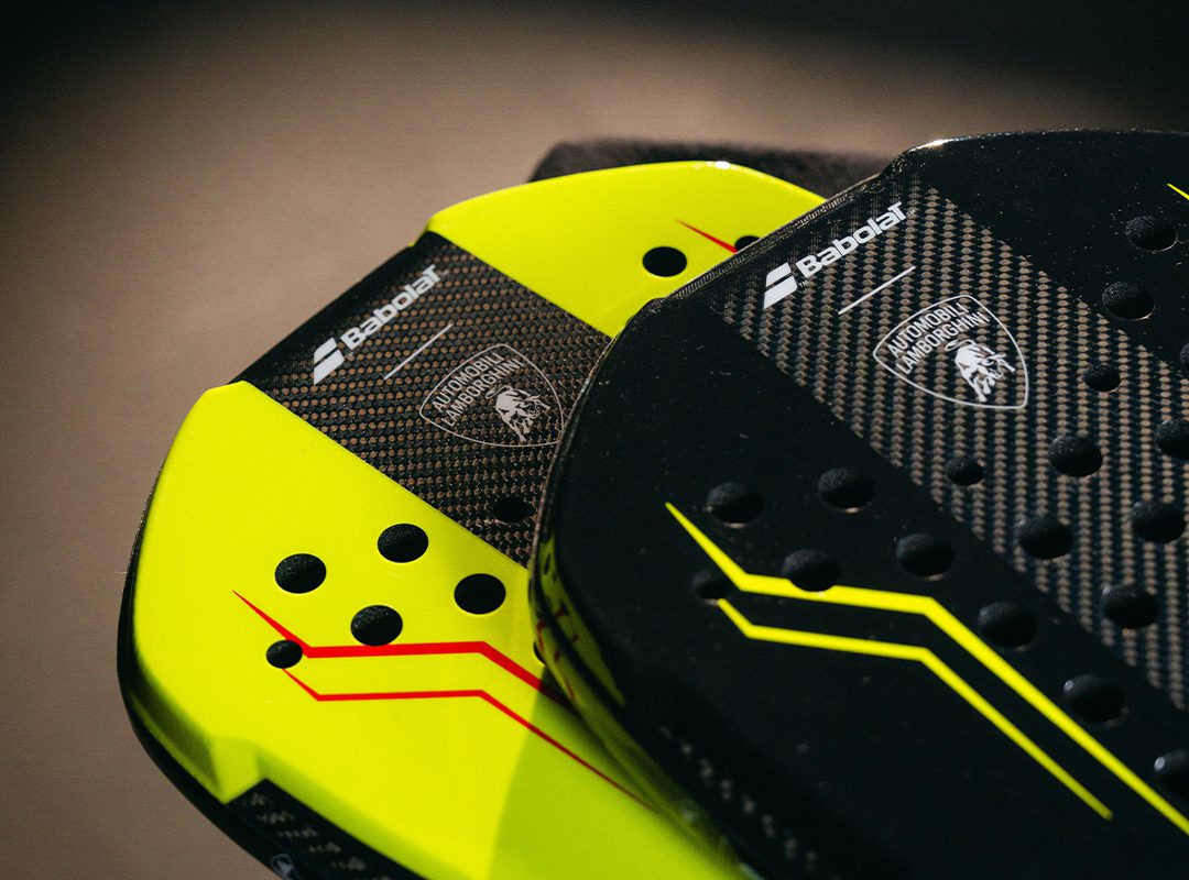 Close-up of two Babolat padel rackets, one yellow and one black, featuring the BL002 Carbon Padel Racquet design with Lamborghini branding and carbon fiber texture.
