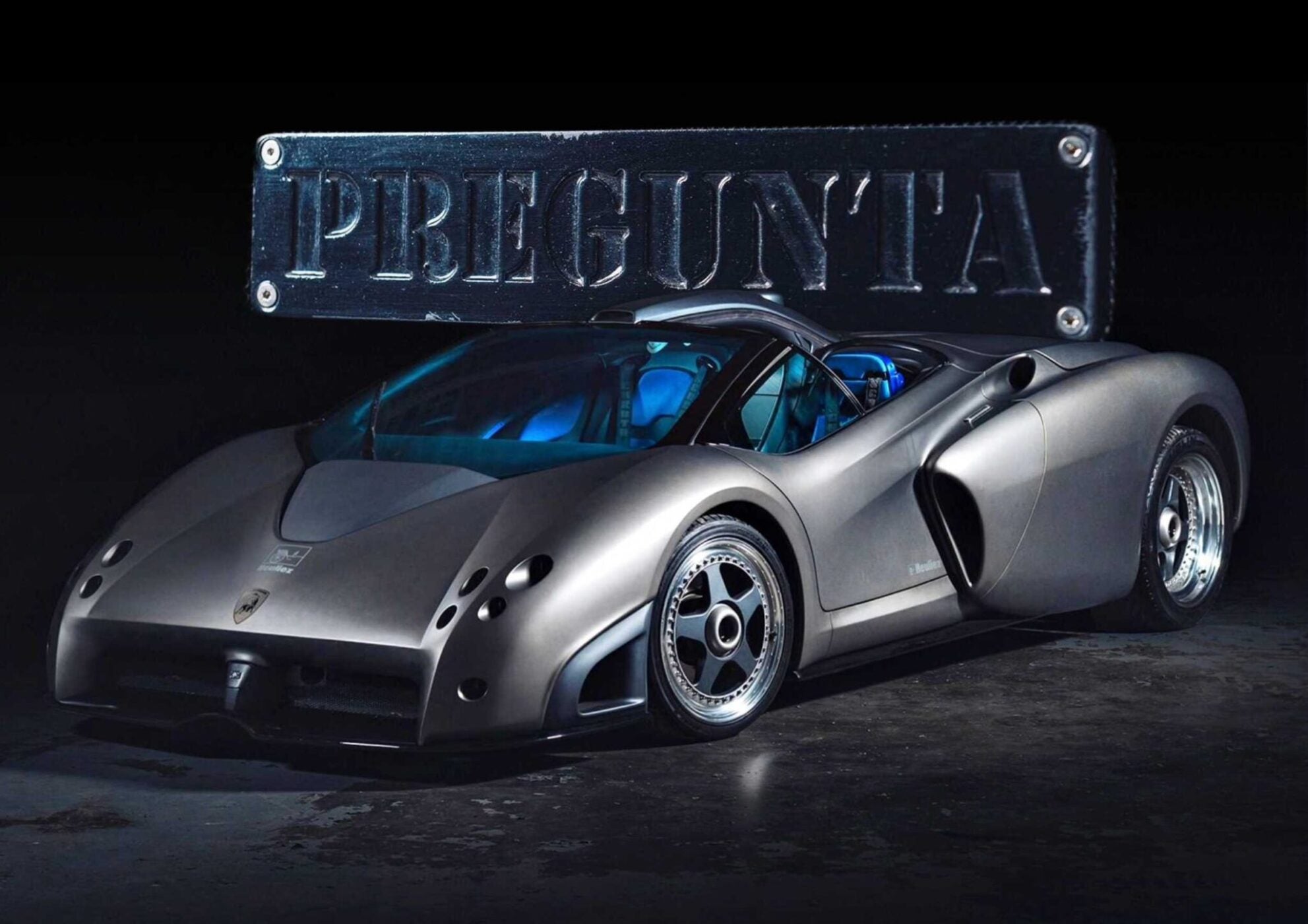 A silver Lamborghini Pregunta concept car is displayed under a sign reading "PREGUNTA" against a dark background, ready for its moment at the upcoming Broad Arrow auction.