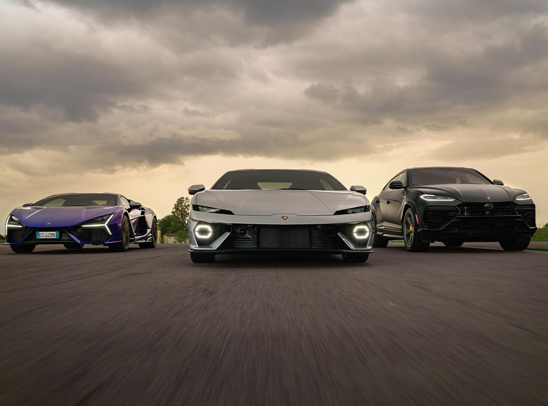 Three luxury vehicles cruise side by side on the highway under a cloudy sky, showcasing a silver Lamborghini from the new car deliveries, a purple sports car, and a black SUV.