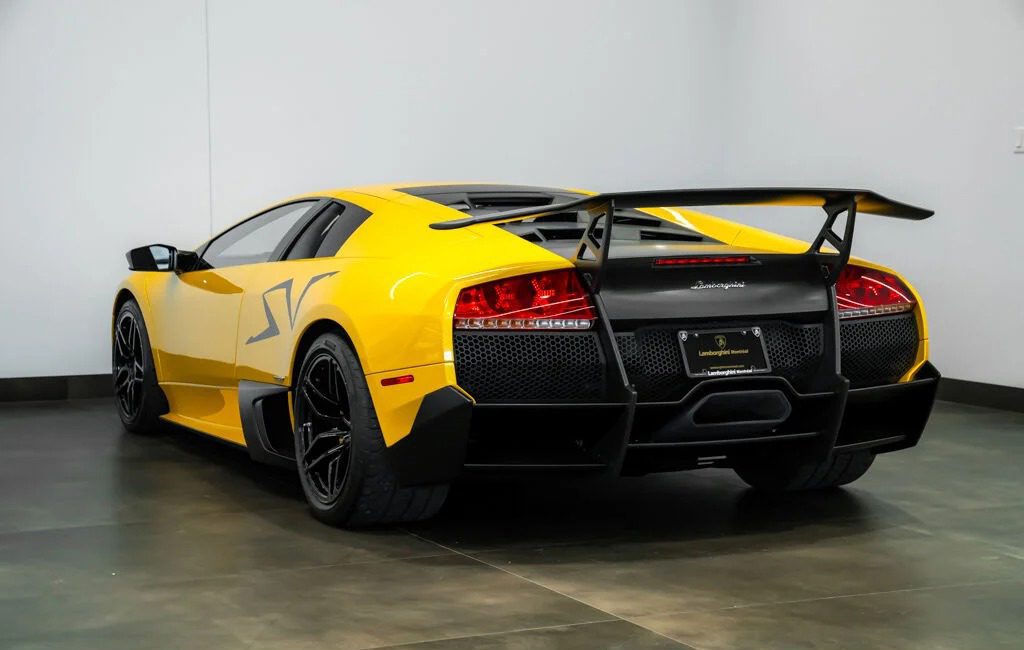 A yellow Lamborghini Murciélago SV sports car is parked indoors, viewed from the rear left angle with a large wing and black accents—an icon among exclusive Lamborghinis. Discover more at Lamborghini Montreal.